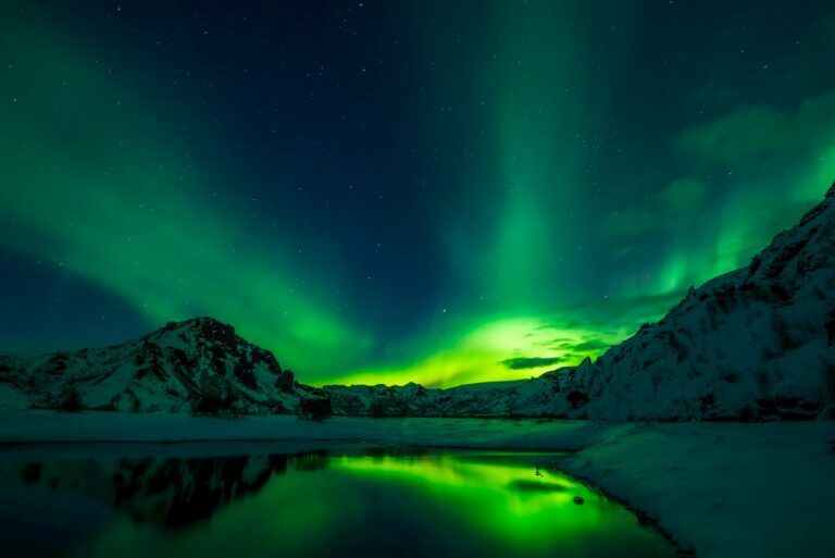 Una espectacular aurora boreal verde ilumina el cielo estrellado sobre montañas nevadas y un lago en Islandia.