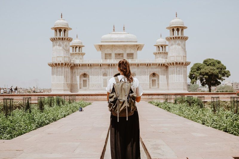 chica con mochila, de espaldas, mirando hacia un edificio en la india
