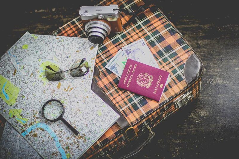 maleta con mapas, maquina de fotos, pasaporte y gafas de sol apoyados encima