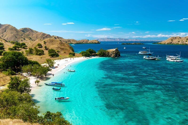playa de indonesia con mar azul, barquitos y montañas al fondo