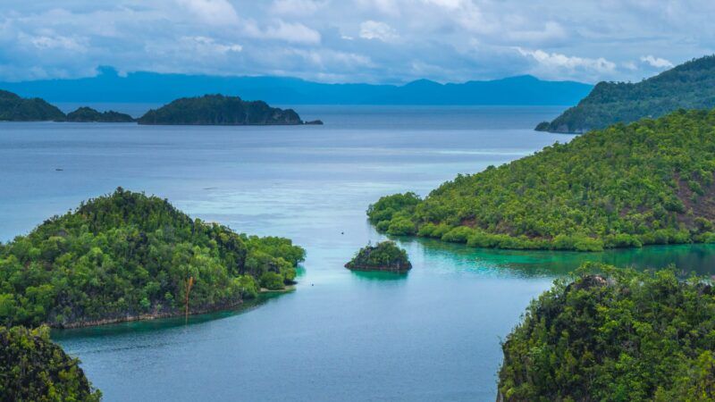 Vista de islas kársticas cubiertas de selva rodeadas de aguas turquesas en Raja Ampat, bajo un cielo nublado.