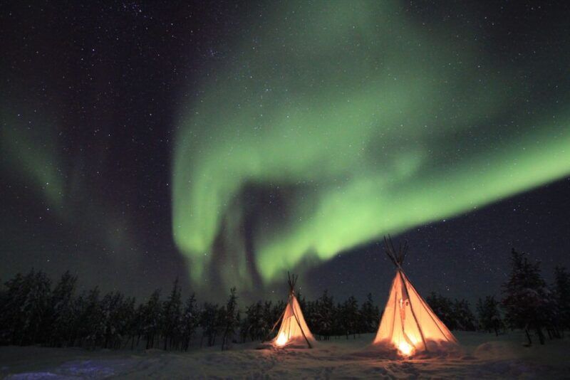 cabañas iluminadas por dentro y aurora boreal, bosque al fondo