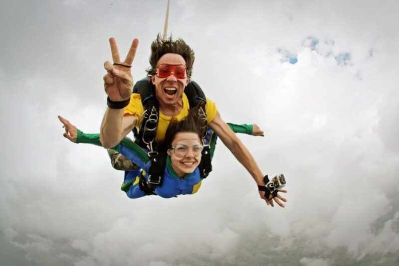 dos personas en el cielo haciendo paracaidismo y mirando a camara