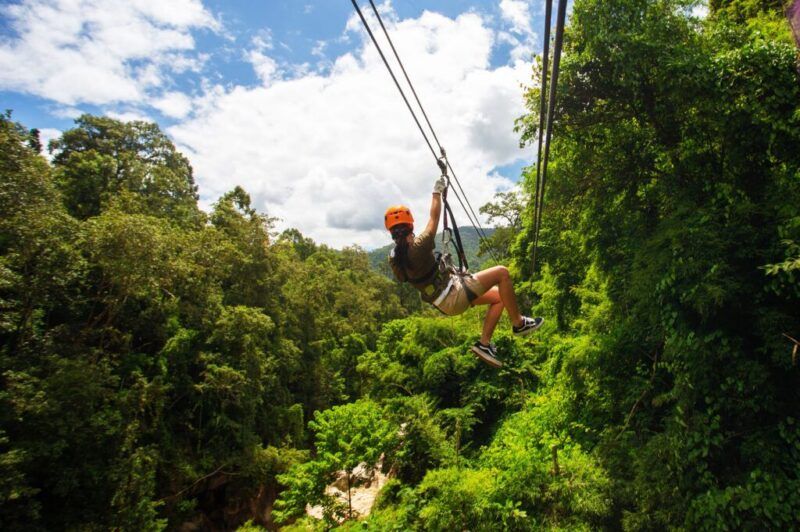 chica de espaldas colgade una zipline en un paisaje verde