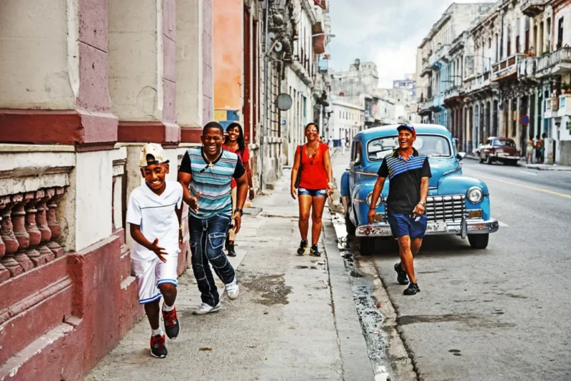 personas corriendo por las calles de cuba, un coche de epoca al fondo