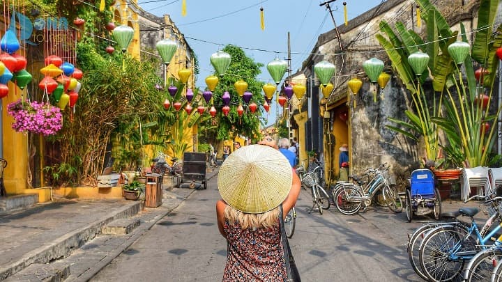 chica de espaldas con sobrero vietnamita sacando foto a calle decorada con lamparas y bicicletas coloridas