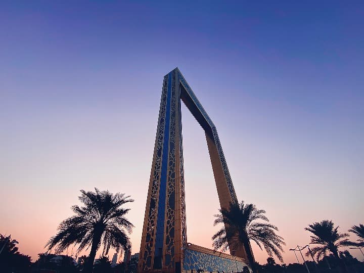 dubai frame visto desde tierra con cielo rosado del atardecer, al lado palmeras - weroad