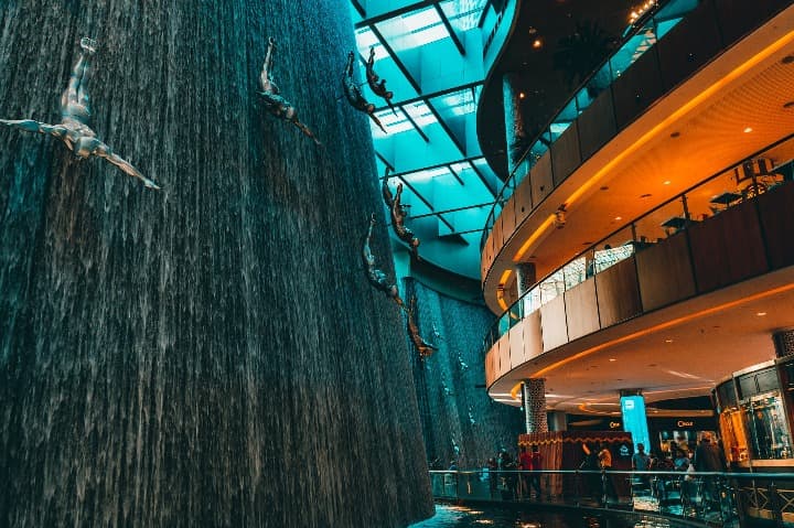 fuente en el interior del dubai mall, se aprecian esculturas que representan chicos saltando al vacio - weroad