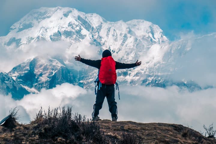 persona de espaldas con mochila roja y brazos abiertos mientras mira el annapurna cubierto de nieve - weroad