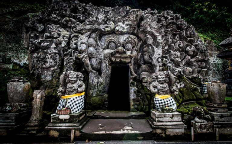 entrada del templo de goa gajah en bali, dos estatuas tienen un telo de color blanco, negro y amarillo