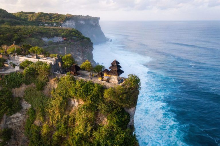 templo de uluwatu visto desde el cielo, se aprecia acantilado frondoso y mar a la derecha