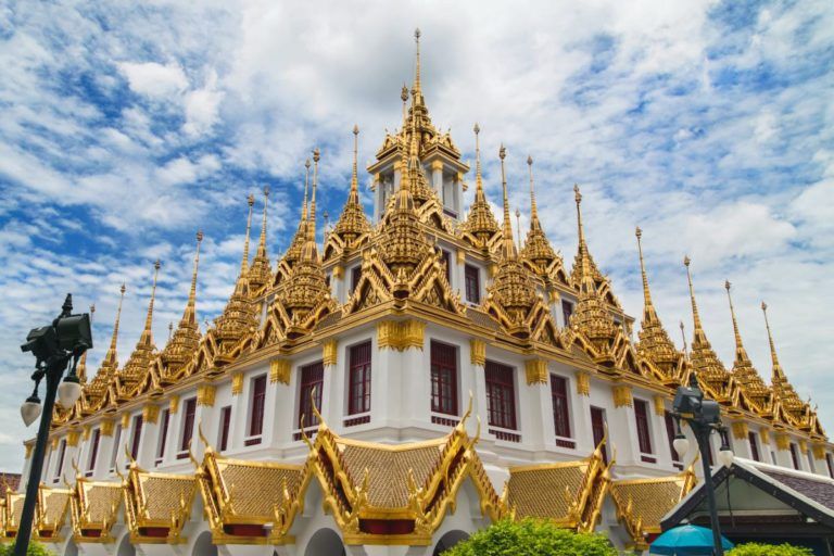 templo de wat ratchanadda con su techo con detalles dorados, detrás cielo azul con nubes - weroad