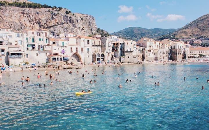 playa de cefalu con gente bañandose, al fondo edificios bajos y detrás montañas - weroad