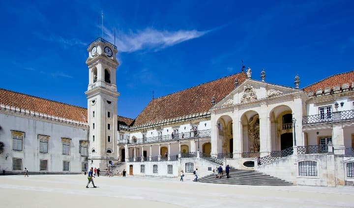 universidad de coimbra, entrada del edificio blanco con techo naranja con torre con reloj - weroad