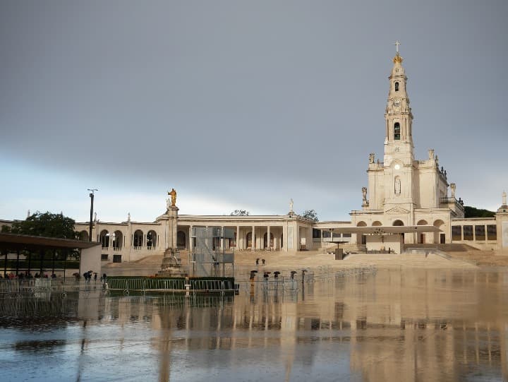 santuario de fátima, portugal, detrás cielo gris y delante suelo mojado que refleja el edificio - weroad