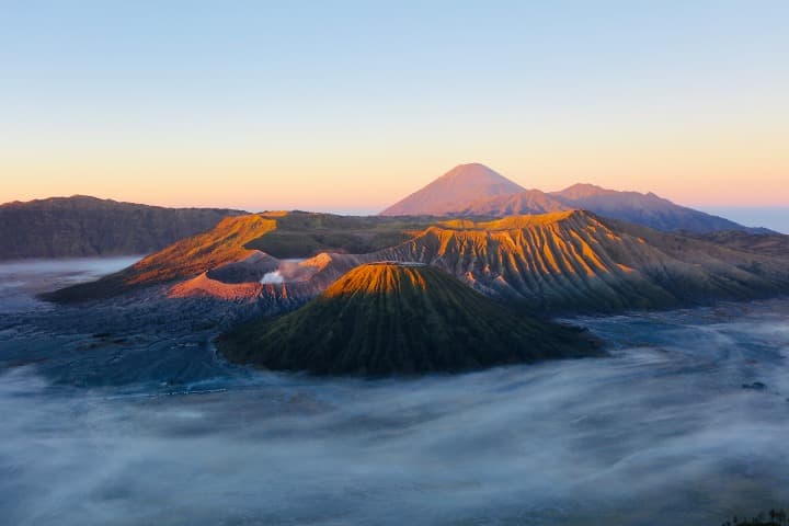 monte bromo visto desde lejos iluminado por el sol con una luz rosada, una de las cosas que ver en indonesia - weroad