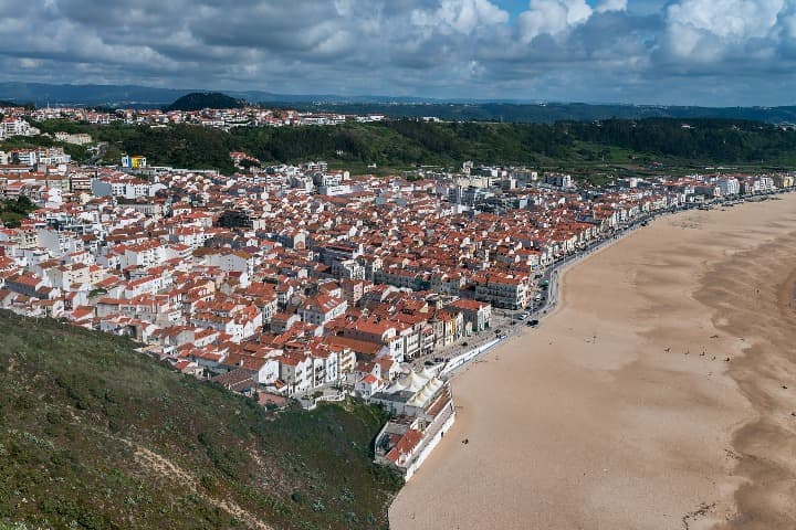 playa y ciudad de nazare vista desde arriba, se aprecian a los lados de los edificios unas montañas verdes - weroad