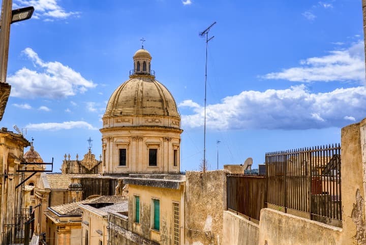 cúpula de una iglesia en el casco antiguo de noto, sicilia, detrás cielo azul y nubes - weroad