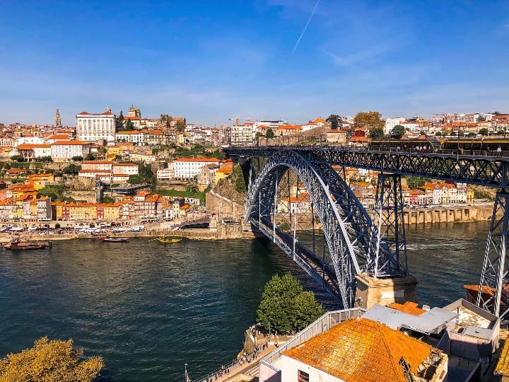 vista de la ciudad de oporto, en portugal, desde la orilla del rio, se aprecia un puente y edificios blancos con techos naranja - weroad