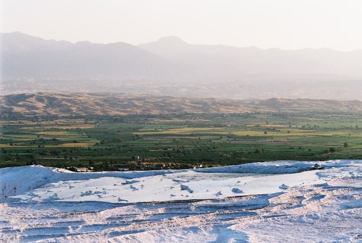 en primer plano, las piscinas naturales de pamukkale; al fondo, paisaje verde y montañas - weroad