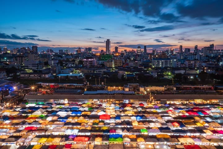 mercado de mae klong en yakarta visto desde arriba, paradas de colores y al fondo los edificios de la ciudad - weroad