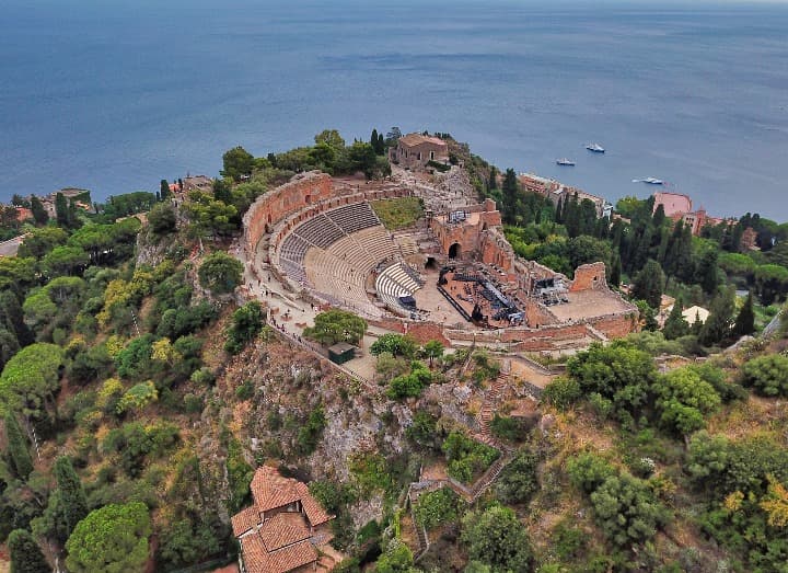 teatro de taormina fotografiado desde el cielo, alrededor arboles y al fondo el mar - weroad
