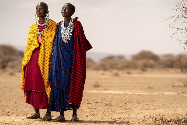 dos maasai vestidos con ropa típica y colorida en medio de un paisaje seco de tanzania - weroad