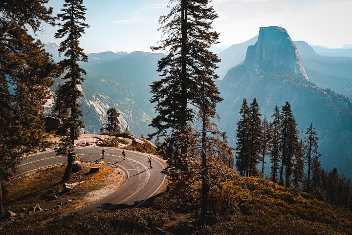 vista de una curva de carretera en glacier point, alrededor arboles y montañas al fondo - weroad
