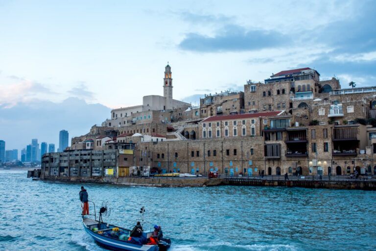 vista de old jaffa desde el agua, edificios bajos de la ciudad antigua, al fondo rascacielos, en primer plano un barquito - weroad