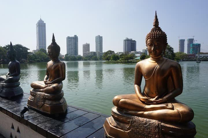 sri lanka qué ver, estatuas de buda con dentrás skyline de la ciudad de colombo, rascacielos y agua - weroad
