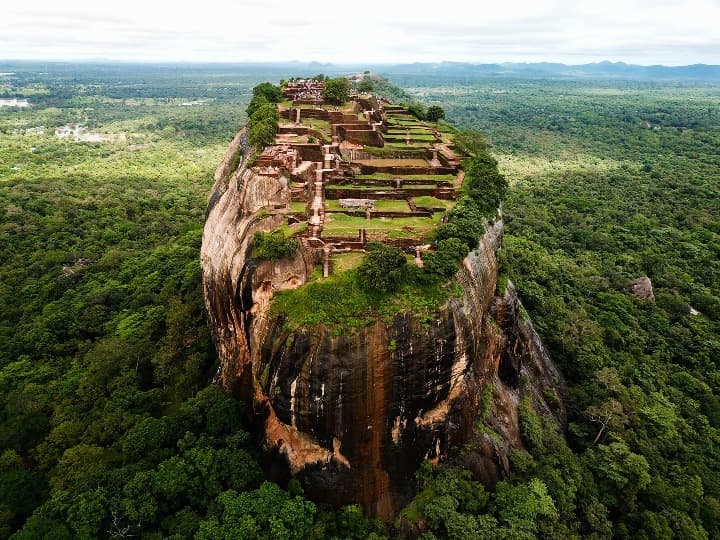 vista aerea de la ciudad de sigiriya construida sobre una roca enorme y empinada, vegetación alrededor - weroad