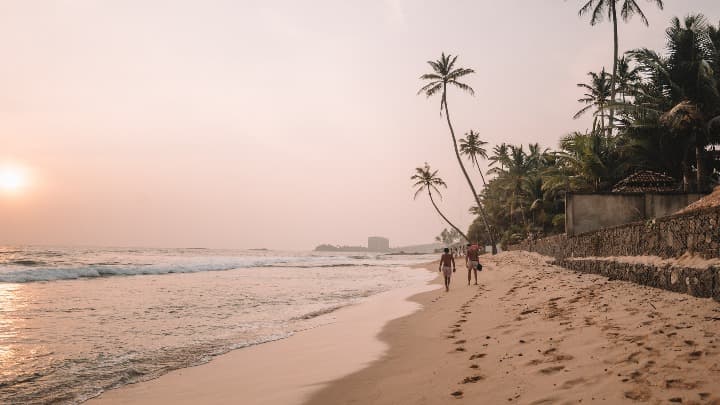 playa de unawatuna al atardecer, palmeras y dos personas caminando por la orilla - weroad