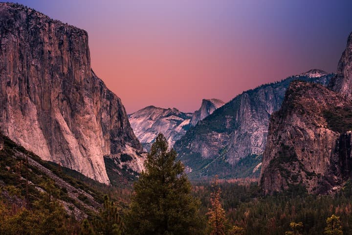 valle de yosemite al atardecer con cielo rosado y arboles en primer plano - weroad