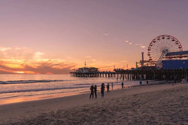 playa de santa mónica, en california al atardecer. persona en la orilla, rueda panorámica detrás - weroad