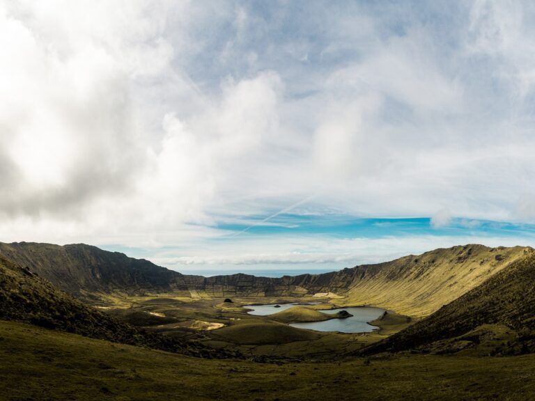 vista de una pradera en isla de corvo, en azores, con un lago al centro y mar al fondo - weroad