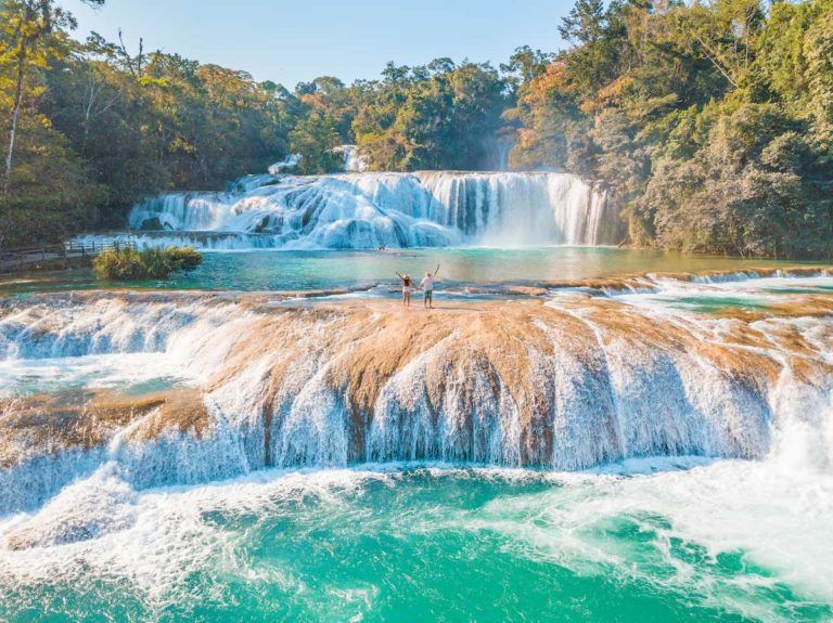 dos chicos dándose la mano en medio de una cascada en agua azul en chiapas, mexico - weroad