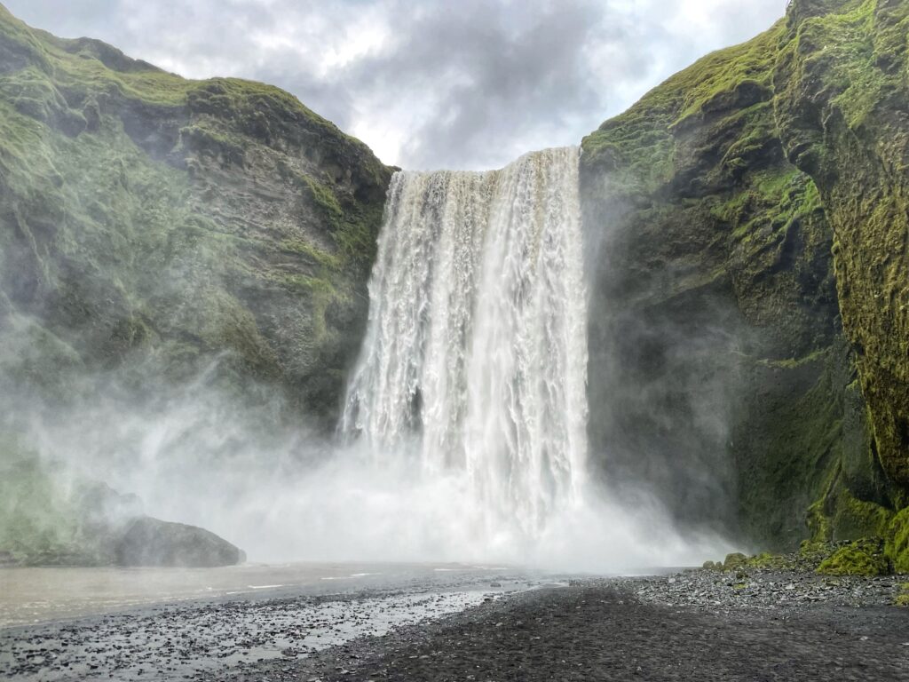 cascada de skógafoss, agua ayendo desde una montaña de color verde - weroad