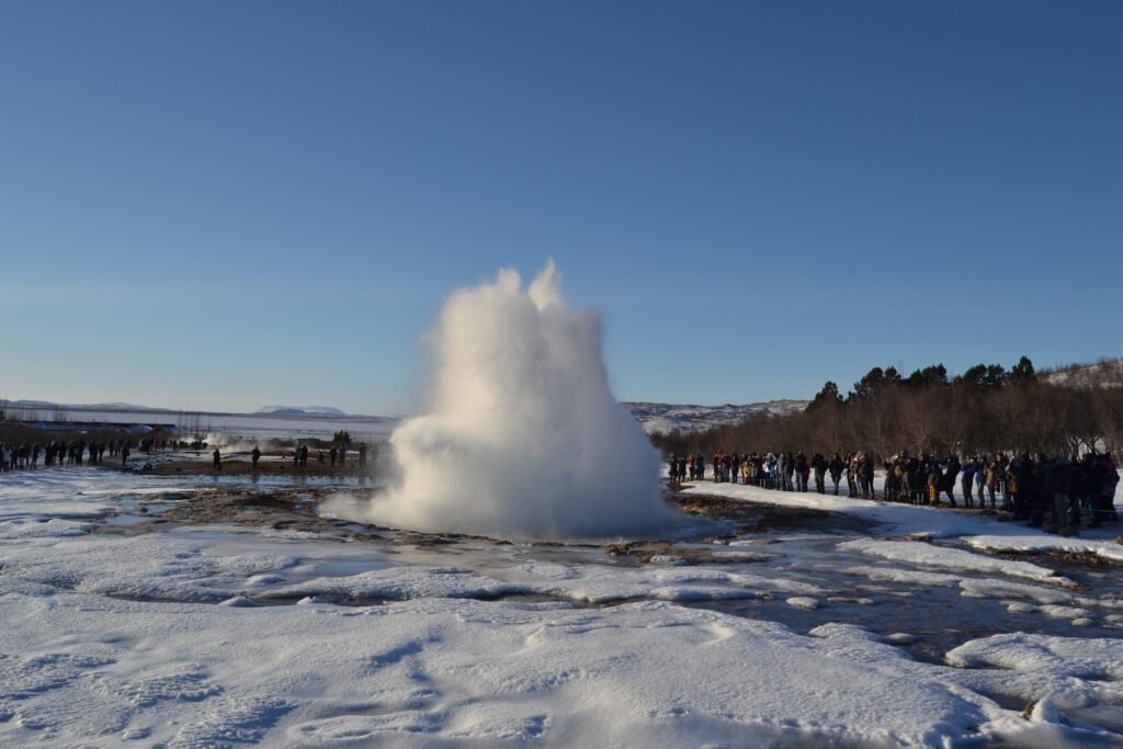 un geyser en una palude helada, de fondo arboles y cielo azul - weroad