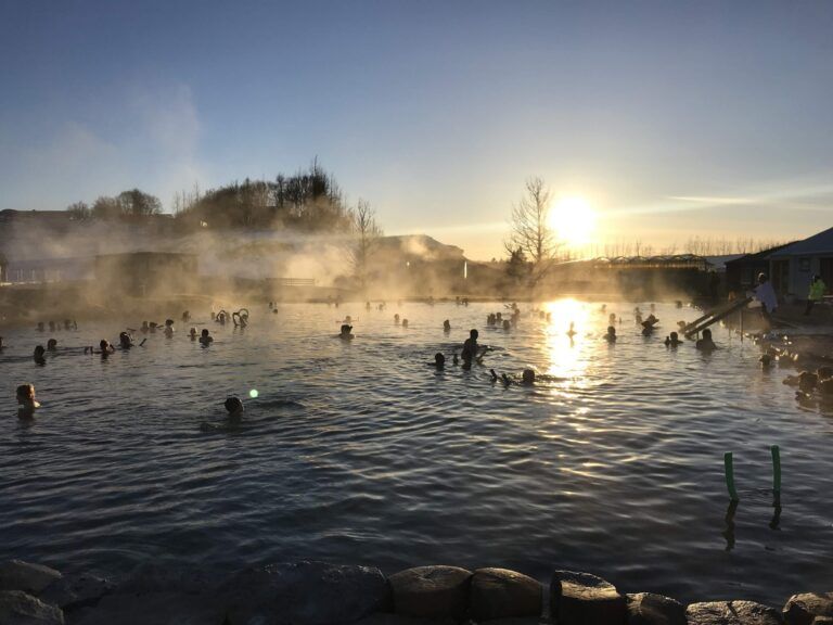 Gente bañandose en una laguna con agua de la que sale humo, al atardecer
