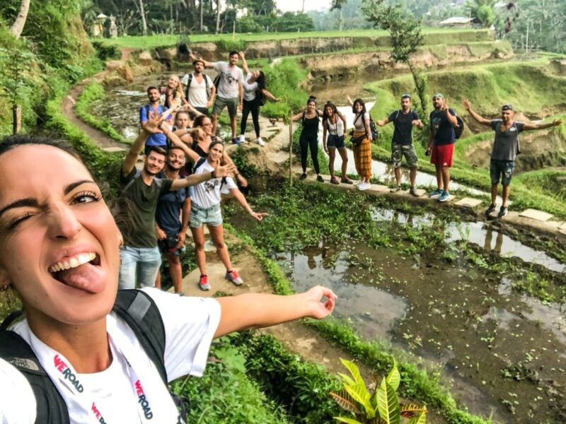 Selfie de coordinadora weroad con detrás otros viajeros en un arrozal en indonesia.