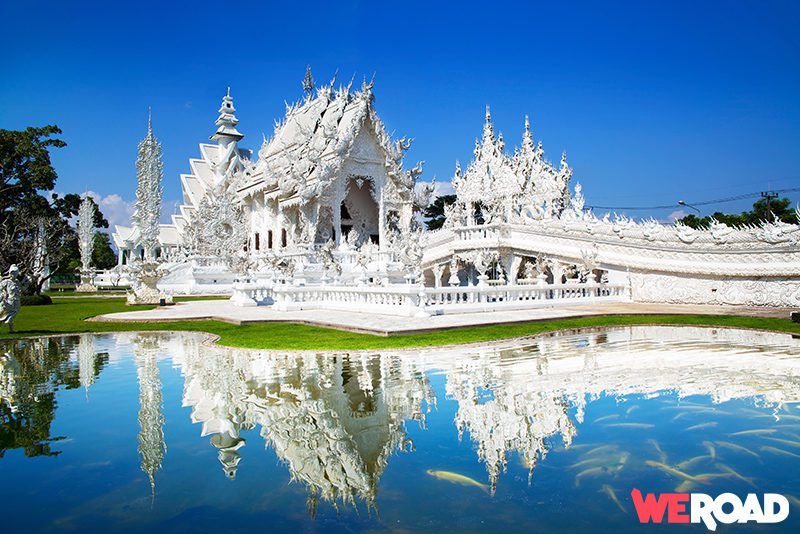 templo blanco wat rong khun que se refleja en un espejo de agua a sus piés, cielo azul detrás - weroad