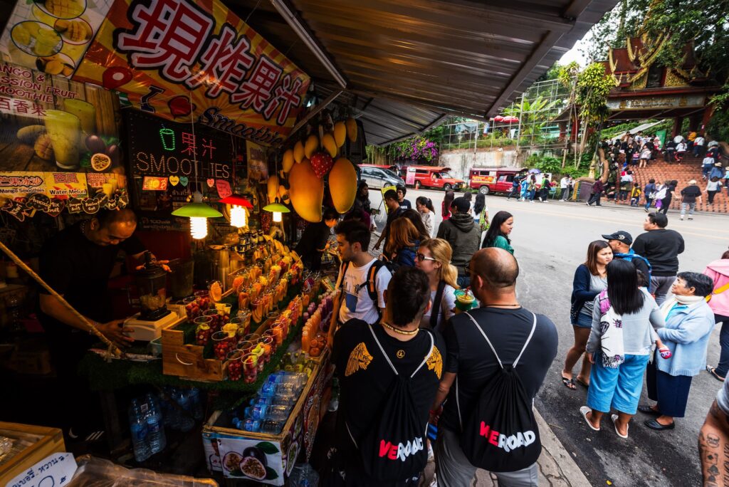 dos viajeros de weroad con sus mochilas, de espaldas, delante de una parada de street food en un mercado, algo que ver en bangkok