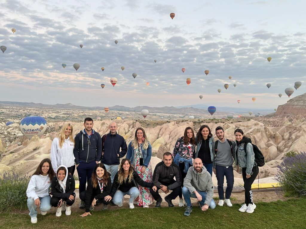 grupo de viajeros weroad con dentrás goreme y cielo lleno de globos aerostáticos volando