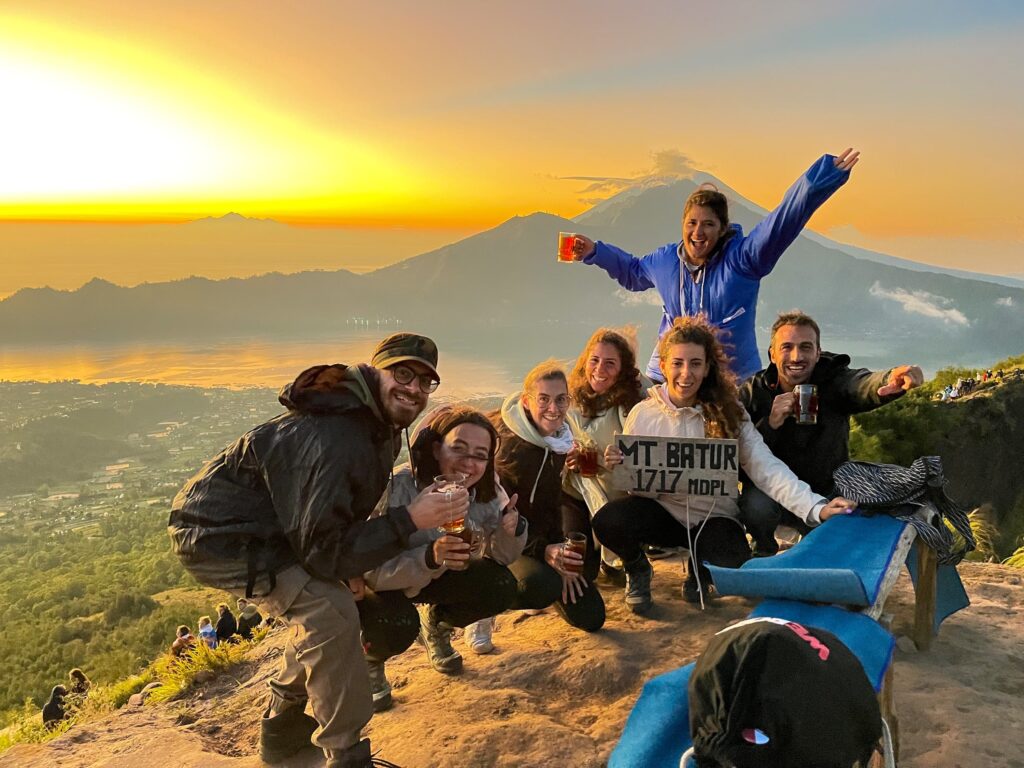 viajeros de weroad bebiendo cerveza con un cartel en la cima del monte batur en indonesia, detrás montañas y puesta del sol