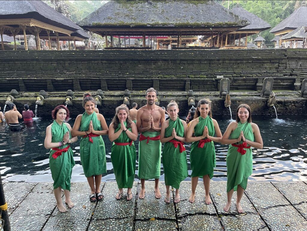 Siete viajeros de weroad mirando a cámara con detrás fuentes del tirta empul, templo que ver en bali