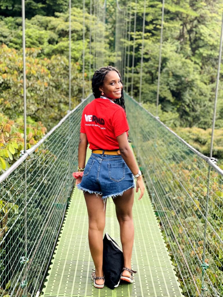chica de espaldas mirando a cámara con camiseta roja de weroad en un puente en costa rica