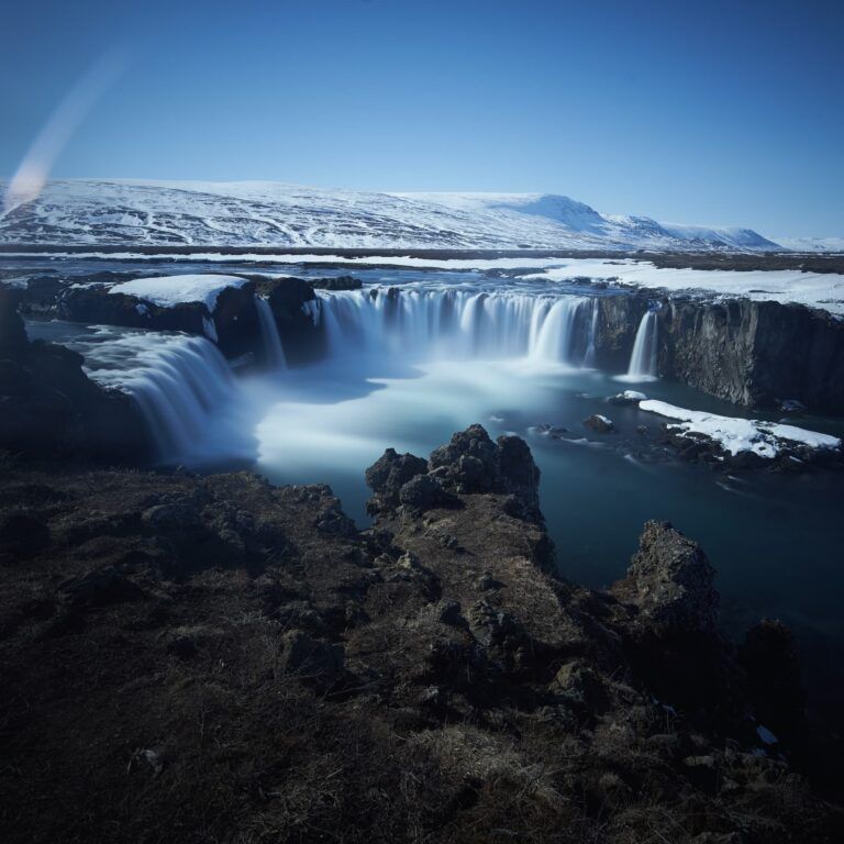 cascada de godafoss vista desde el cielo, alrededor formaciones rocosas y montañas detrás - weroad