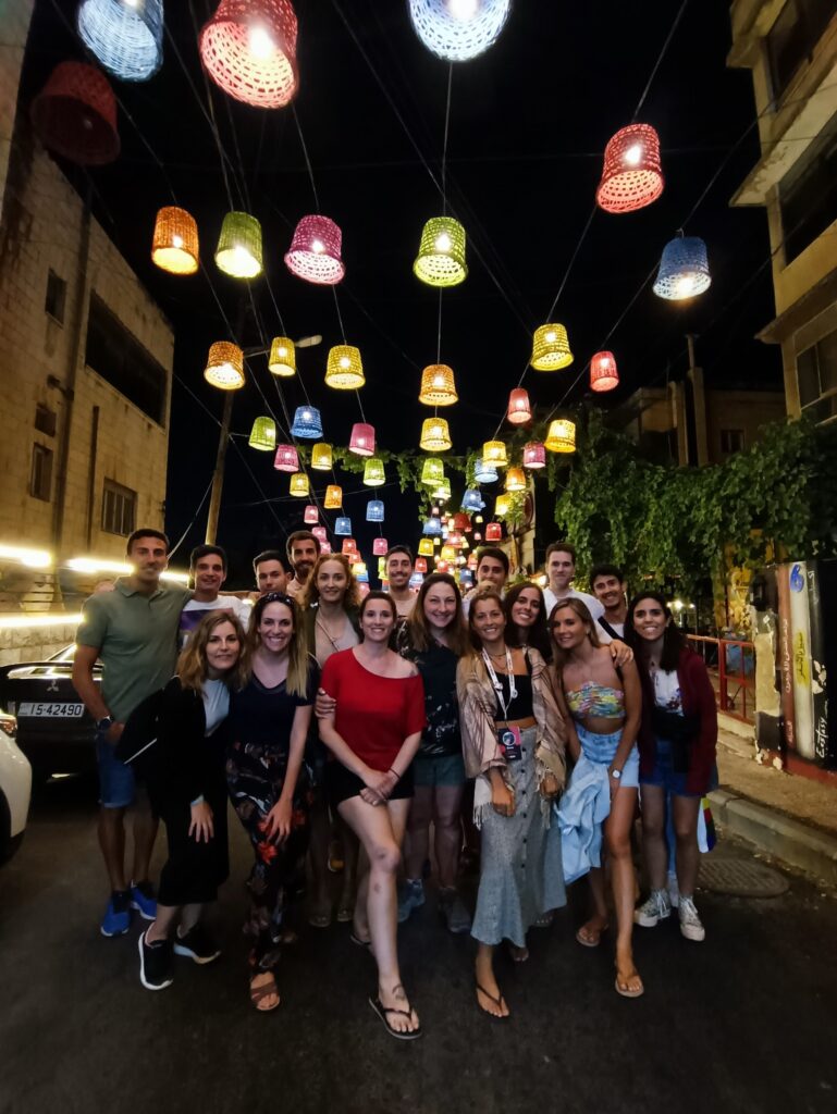 foto de grupo de viajeros de weroad en rainbow street en ammán, con luces de colores colgando encima de la calle