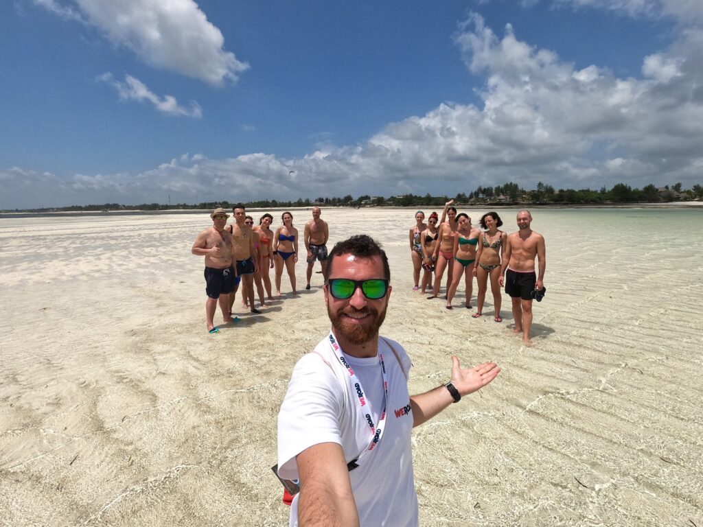 selfie de un coordinador de weroad con detrás viajeros en una playa de zanzibar,  sitio donde viajar en invierno