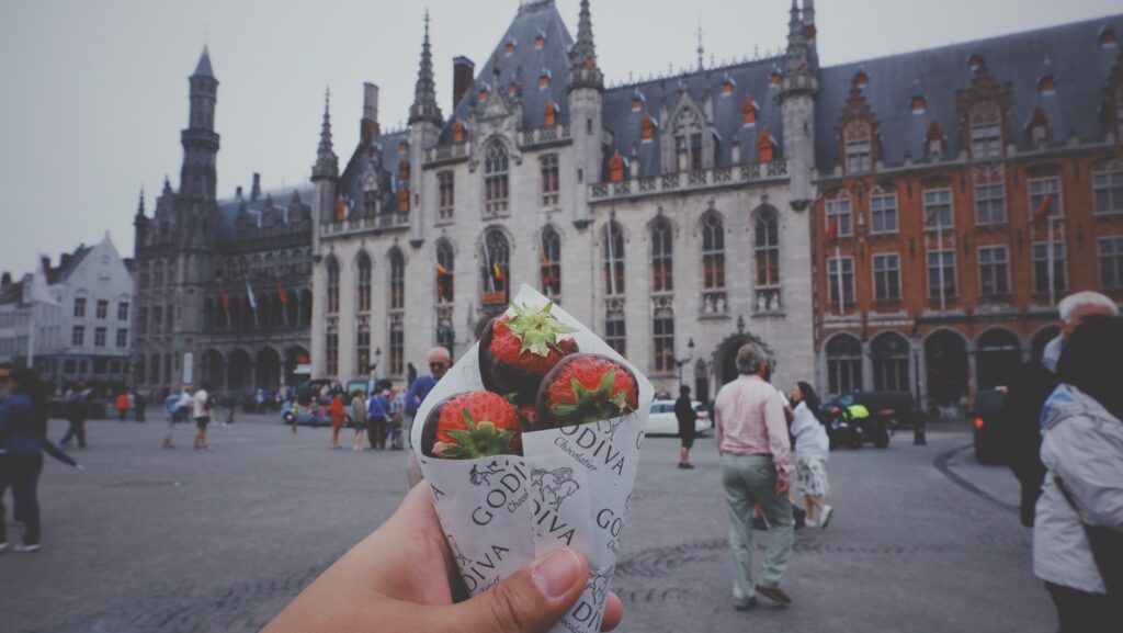 cucurucho de fresas con chocolate de la marca godiva, detrás un edificio del centro de brujas - weroad